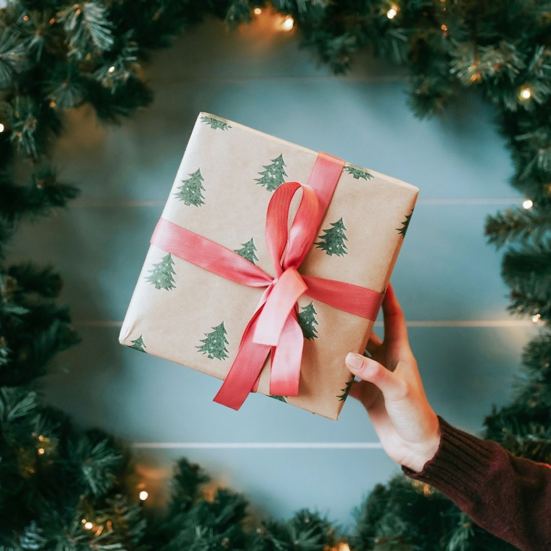 Eco Friendly Secret Santa Gifts - hand holding Christmas gift with foliage behind